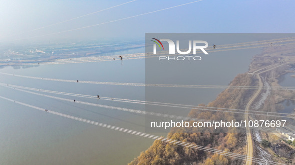 Construction workers are performing an acceptance check on the 200 kV DC transmission line project, which is 100 meters high, in Yangzhou, J...