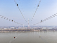 Construction workers are performing an acceptance check on the 200 kV DC transmission line project, which is 100 meters high, in Yangzhou, J...