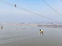 Construction workers are performing an acceptance check on the 200 kV DC transmission line project, which is 100 meters high, in Yangzhou, J...