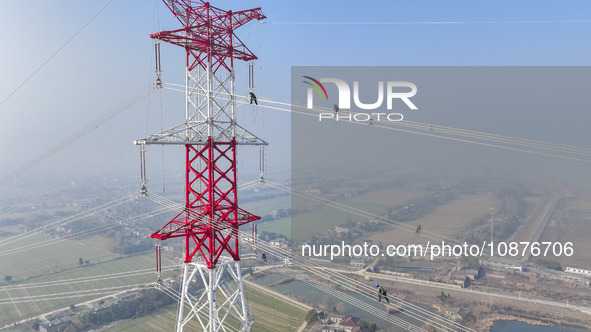 Construction workers are performing an acceptance check on the 200 kV DC transmission line project, which is 100 meters high, in Yangzhou, J...