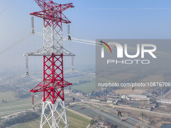 Construction workers are performing an acceptance check on the 200 kV DC transmission line project, which is 100 meters high, in Yangzhou, J...