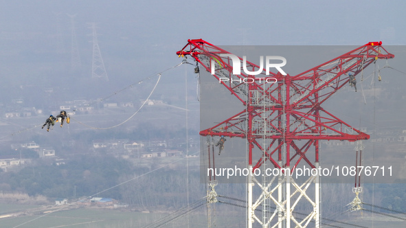 Construction workers are performing an acceptance check on the 200 kV DC transmission line project, which is 100 meters high, in Yangzhou, J...