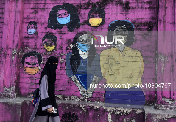 A Muslim woman is walking past a mural painting of faces wearing masks amid a sudden surge of the JN.1 coronavirus in Mumbai, India, on Janu...