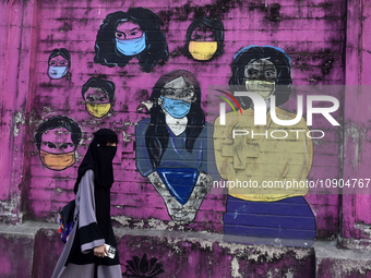 A Muslim woman is walking past a mural painting of faces wearing masks amid a sudden surge of the JN.1 coronavirus in Mumbai, India, on Janu...