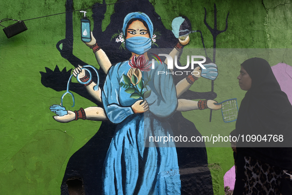 A Muslim woman is walking past a mural painting of a face wearing masks amid a sudden surge of the JN.1 coronavirus in Mumbai, India, on Jan...