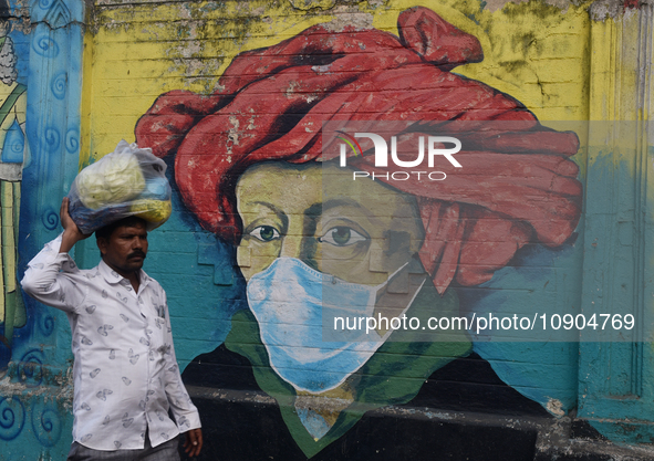 A man is walking past a mural painting of a face wearing masks amid a sudden surge of the JN.1 coronavirus in Mumbai, India, on January 11,...