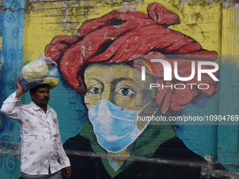 A man is walking past a mural painting of a face wearing masks amid a sudden surge of the JN.1 coronavirus in Mumbai, India, on January 11,...