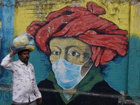 A man is walking past a mural painting of a face wearing masks amid a sudden surge of the JN.1 coronavirus in Mumbai, India, on January 11,...