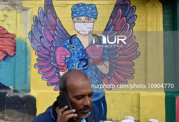 A man is talking on his phone while walking past a mural painting of a doctor wearing masks amid a sudden surge of the JN.1 coronavirus in M...