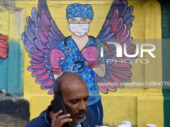 A man is talking on his phone while walking past a mural painting of a doctor wearing masks amid a sudden surge of the JN.1 coronavirus in M...