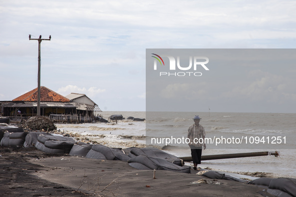 Carmat (83) is walking on the beach near the remains of his house, which was destroyed by high waves in Cemarajaya Village, Karawang Regency...