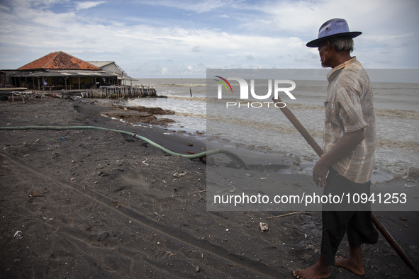 Carmat (83) is walking on the beach near the remains of his house, which was destroyed by high waves in Cemarajaya Village, Karawang Regency...