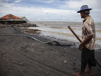 Carmat (83) is walking on the beach near the remains of his house, which was destroyed by high waves in Cemarajaya Village, Karawang Regency...