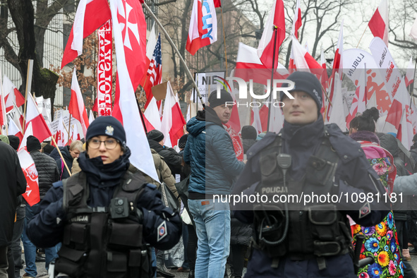 Police officers guard a crowd of people, holding Polish national flag and anti-government banners, led by far right media - Gazeta Polska an...