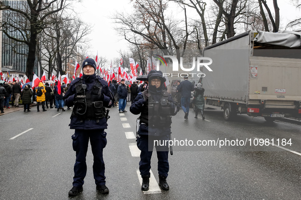 Police officers guard a crowd of people, holding Polish national flag and anti-government banners, led by far right media - Gazeta Polska an...