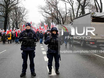 Police officers guard a crowd of people, holding Polish national flag and anti-government banners, led by far right media - Gazeta Polska an...