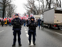 Police officers guard a crowd of people, holding Polish national flag and anti-government banners, led by far right media - Gazeta Polska an...