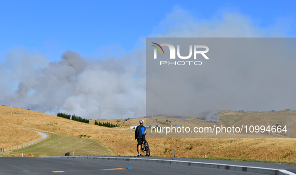 A cyclist is looking at the thick smoke that is rising from a fire in Christchurch, New Zealand, on February 14, 2024. A local state of emer...