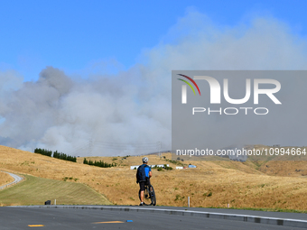 A cyclist is looking at the thick smoke that is rising from a fire in Christchurch, New Zealand, on February 14, 2024. A local state of emer...