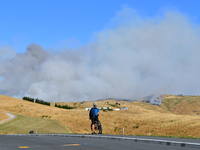 A cyclist is looking at the thick smoke that is rising from a fire in Christchurch, New Zealand, on February 14, 2024. A local state of emer...