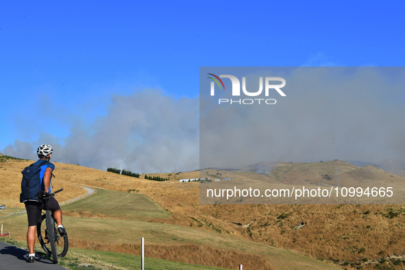 A cyclist is looking at the thick smoke that is rising from a fire in Christchurch, New Zealand, on February 14, 2024. A local state of emer...