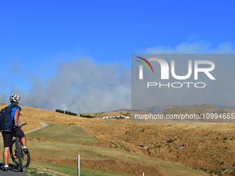 A cyclist is looking at the thick smoke that is rising from a fire in Christchurch, New Zealand, on February 14, 2024. A local state of emer...