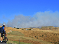 A cyclist is looking at the thick smoke that is rising from a fire in Christchurch, New Zealand, on February 14, 2024. A local state of emer...