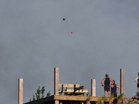 A fire-fighting helicopter is flying over an area of burning vegetation, working to extinguish a wildfire in Christchurch, New Zealand, on F...