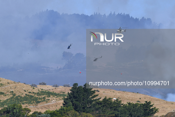 Fire-fighting helicopters are flying over an area of burning vegetation as they work to put out a wildfire in Christchurch, New Zealand, on...