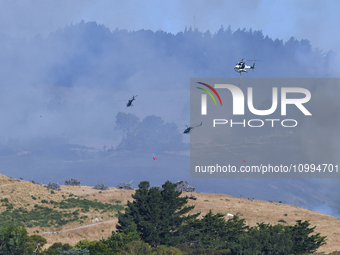 Fire-fighting helicopters are flying over an area of burning vegetation as they work to put out a wildfire in Christchurch, New Zealand, on...