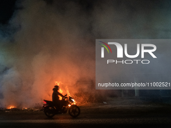 A motorcyclist is riding past burning garbage on a busy road in Dhaka, Bangladesh, on February 17, 2024. Five of the top 10 causes of death...