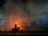 A motorcyclist is riding past burning garbage on a busy road in Dhaka, Bangladesh, on February 17, 2024. Five of the top 10 causes of death...