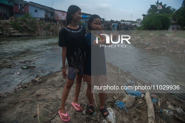 Two teenage girls are posing with their cellphones in the Deli River, which is polluted by plastic waste, in Medan, North Sumatra, Indonesia...