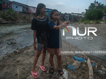 Two teenage girls are posing with their cellphones in the Deli River, which is polluted by plastic waste, in Medan, North Sumatra, Indonesia...