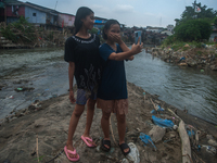 Two teenage girls are posing with their cellphones in the Deli River, which is polluted by plastic waste, in Medan, North Sumatra, Indonesia...