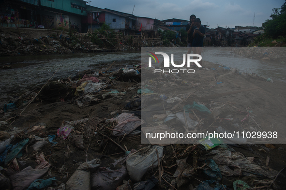 Two teenage girls are posing with their cellphones in the Deli River, which is polluted by plastic waste, in Medan, North Sumatra, Indonesia...