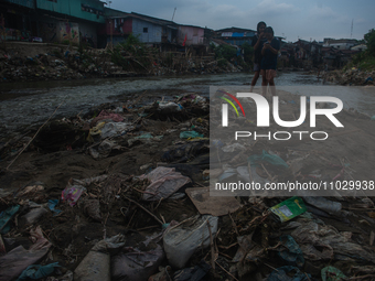 Two teenage girls are posing with their cellphones in the Deli River, which is polluted by plastic waste, in Medan, North Sumatra, Indonesia...