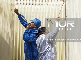 Two workers are processing hollow hanging noodles at a workshop in Suqian, Jiangsu Province, China, on March 3, 2024. (