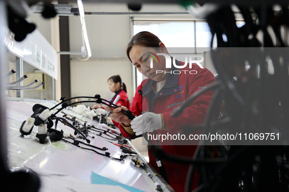 A worker is producing automotive wiring harness products at a workshop of an auto parts manufacturer in Binzhou, Shandong Province, China, o...