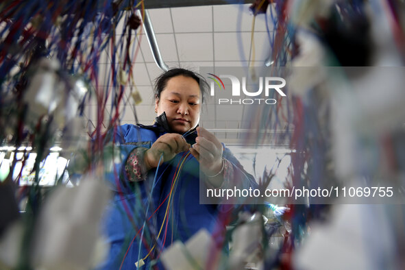 A worker is producing automotive wiring harness products at a workshop of an auto parts manufacturer in Binzhou, Shandong Province, China, o...