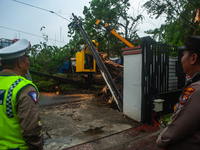 Police personnel are standing guard while officers are cutting trees that fell due to extreme weather in Medan City, North Sumatra, Indonesi...