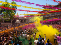 Thousands of devotees are cheering as a priest sprays colored powder and water on them during the celebrations of the colorful Holi festival...