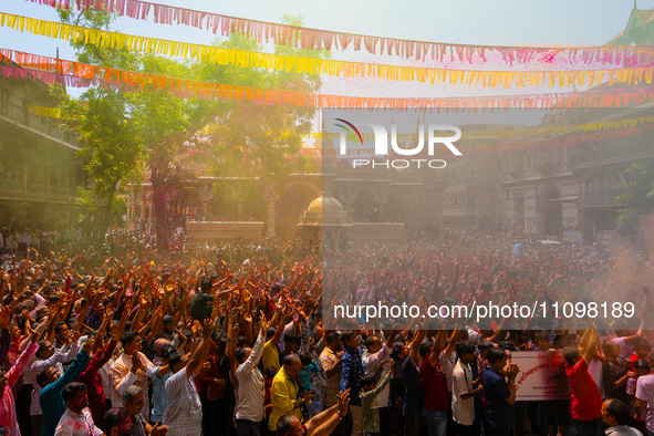 Thousands of devotees are cheering as a priest sprays colored powder and water on them during the celebrations of the colorful Holi festival...