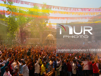 Thousands of devotees are cheering as a priest sprays colored powder and water on them during the celebrations of the colorful Holi festival...