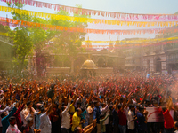 Thousands of devotees are cheering as a priest sprays colored powder and water on them during the celebrations of the colorful Holi festival...