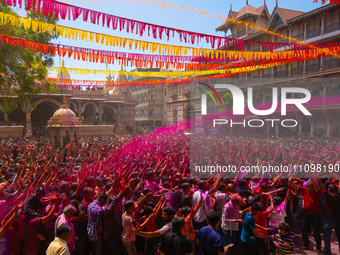 Thousands of devotees are cheering as a priest sprays colored powder and water on them during the celebrations of the colorful Holi festival...