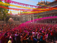 Thousands of devotees are cheering as a priest sprays colored powder and water on them during the celebrations of the colorful Holi festival...