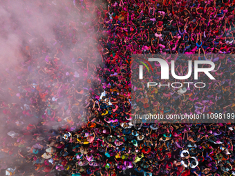 Thousands of devotees are cheering as a priest sprays colored powder and water on them during the celebrations of the colorful Holi festival...