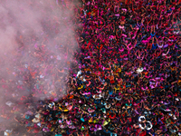 Thousands of devotees are cheering as a priest sprays colored powder and water on them during the celebrations of the colorful Holi festival...