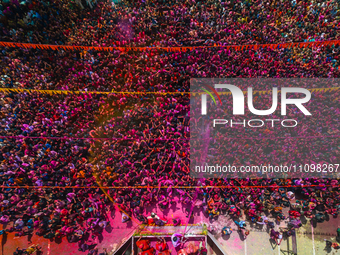 Thousands of devotees are cheering as a priest sprays colored powder and water on them during the celebrations of the colorful Holi festival...